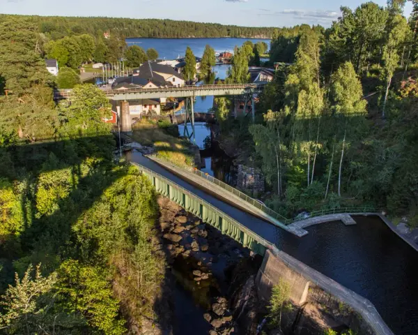 Vattenvägar och akvedukter i Sverige, med gröna broar som leder vatten över en ravin, omgivna av frodig skog och en sjö i bakgrunden.