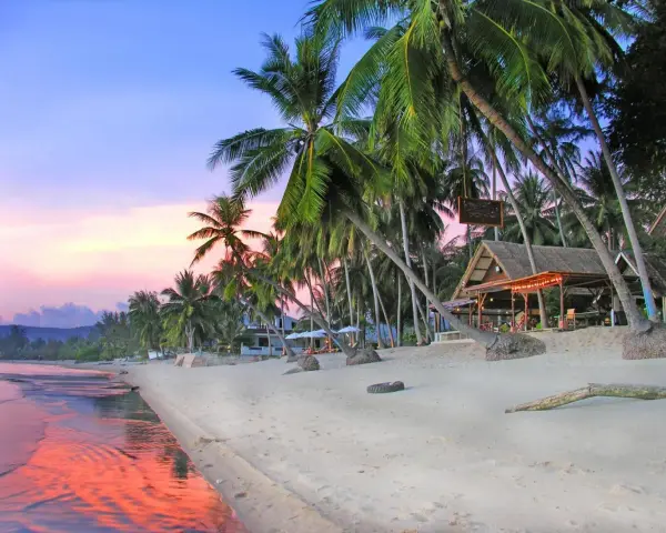 En vacker strand på Koh Samui, Thailand, med vajande palmer, en strandbar och ett hav som speglar den rosa solnedgången.