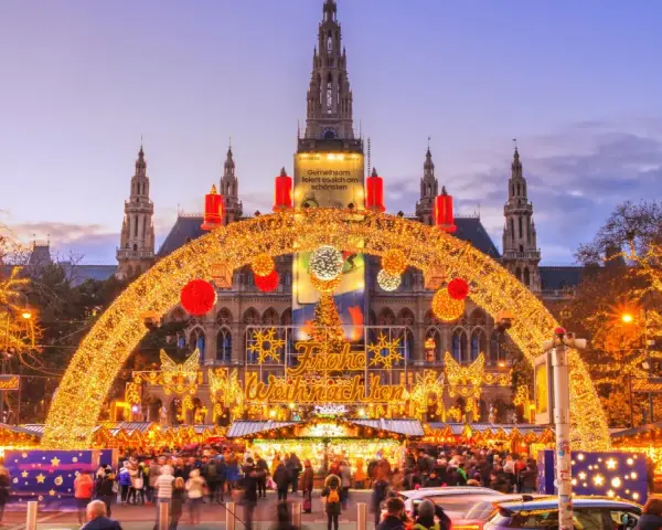 En magisk julmarknad i Wien, med Rådhuset i bakgrunden, gnistrar av tusentals ljus. En båge av gyllene ljusslingor välkomnar besökare till den livliga julmarknaden.