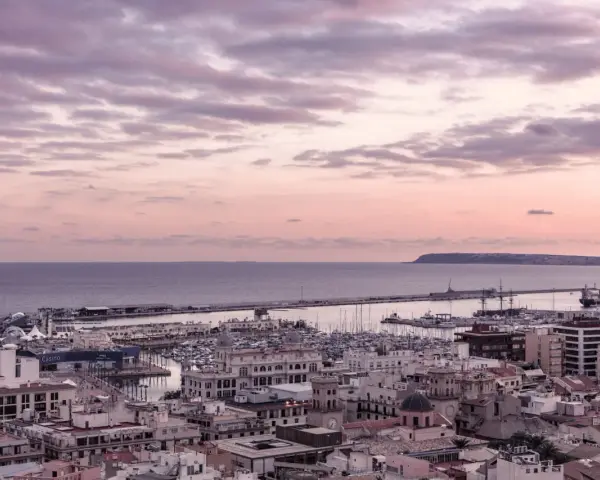 En vacker solnedgång över hamnen i Alicante i december. Molnen färgas i rosa och lila över havet och staden.