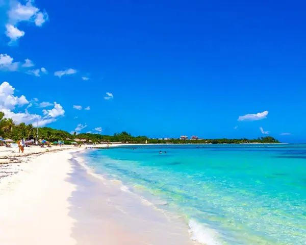Vacker strand med turkost vatten och vita moln. Trots den idylliska vyn, kan Playa del Carmen vara farligt.