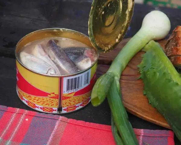 En burk med sill, en klassisk del av **comida tipica sueca**, ligger bredvid färska grönsaker och bröd.
