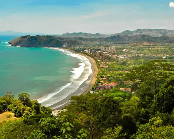 Vacker kustlinje med turkost hav, vågor som slår mot en sandstrand och frodig grönska som omger en stad. En dröm om en costa rica strand.