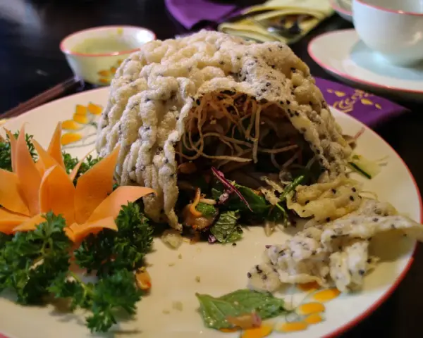 En vacker vietnamesisk maträtt med krispig rispapperstäckt sallad, dekorerad med morotsblomma och örter.