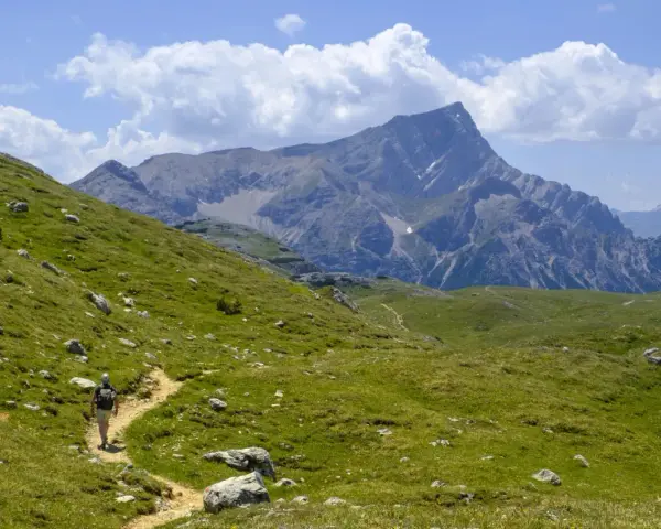 Vandrare på en stig i Dolomiterna, omgiven av gröna sluttningar och majestätiska berg under en molnig himmel.