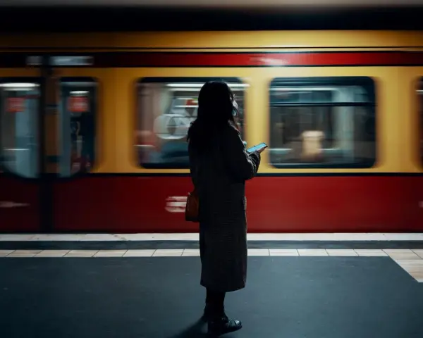 Kvinna med mobil på perrongen i Berlin, en gul och röd tunnelbanevagn susar förbi. Perfekt för din berlin reseguide.