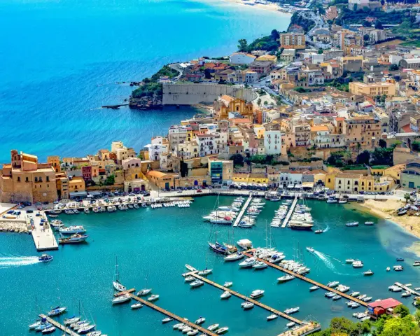 En charmig hamn i Palermo, Sicilien, med färgglada hus och många båtar i det turkosa vattnet.
