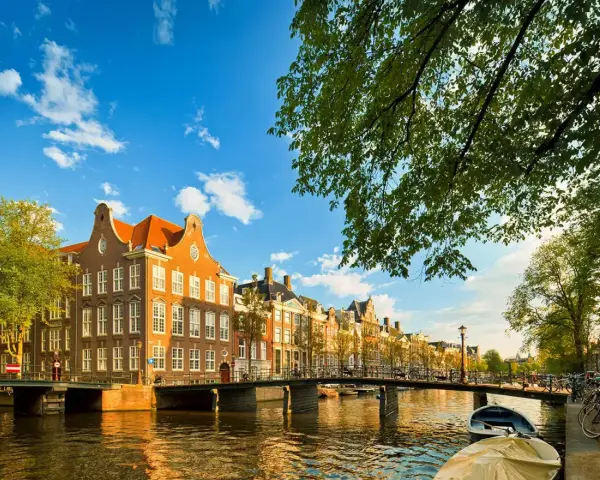 En vacker kanalvy i Amsterdam med klassiska hus, broar och båtar. Perfekt för din amsterdam reseguide.