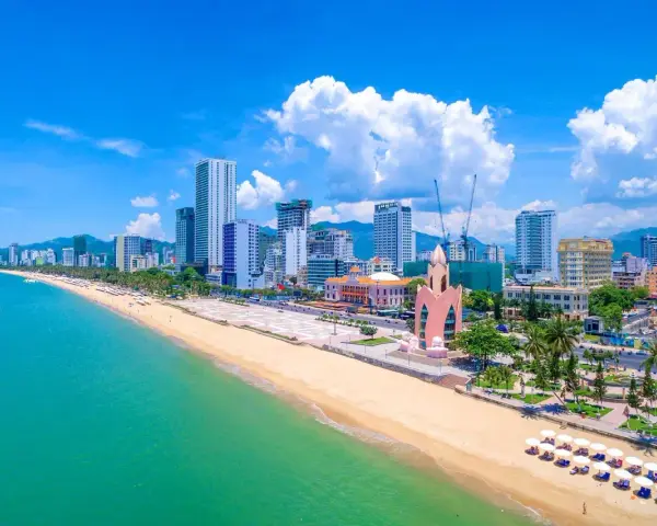 En vidsträckt strand med turkost vatten och en stadssilhuett i bakgrunden. Nha Trang beach är en populär destination.
