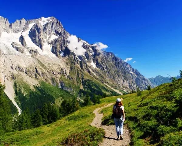 En person vandrar på en stig i Chamonix med majestätiska berg och en glaciär i bakgrunden.