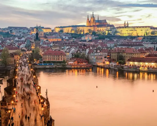 En livlig kväll på Karlsbron i Prag, med tusentals besökare som promenerar mot slottet. En perfekt vy för den som tar tåg till Prag.
