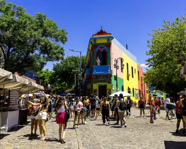 Färgglada hus och marknadsstånd i Buenos Aires. En livlig gata med människor som njuter av solen.