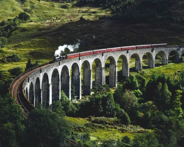 Ångloket på Glenfinnanviadukten i Skottland, som påminner om Harry Potter tåg skottland, ångar fram över den gröna dalen.