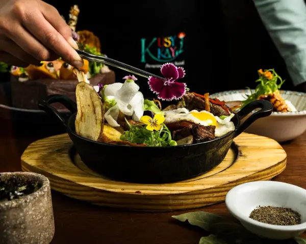 En hand dekorerar en mustig gryta med kött, potatis och blommor. En utsökt rätt som påminner om kanadensiskt kök.