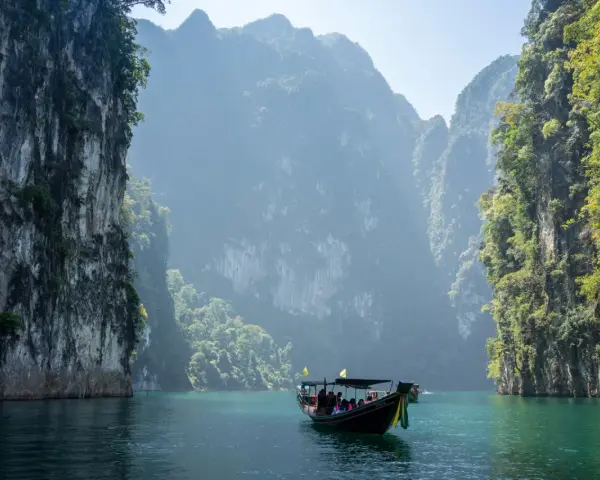 En båt färdas på turkost vatten genom dramatiska kalkstensklippor i Khao Sok nationalpark.