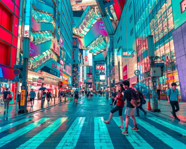 Neonbelyst gata i Tokyo, perfekt för din tokyo reseguide. Människor promenerar under paraplyer i regnet bland blinkande skyltar.