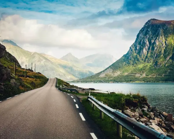 Väg som slingrar sig genom dramatiskt landskap med berg och fjord. En drömresa till Lofoten från Stockholm.