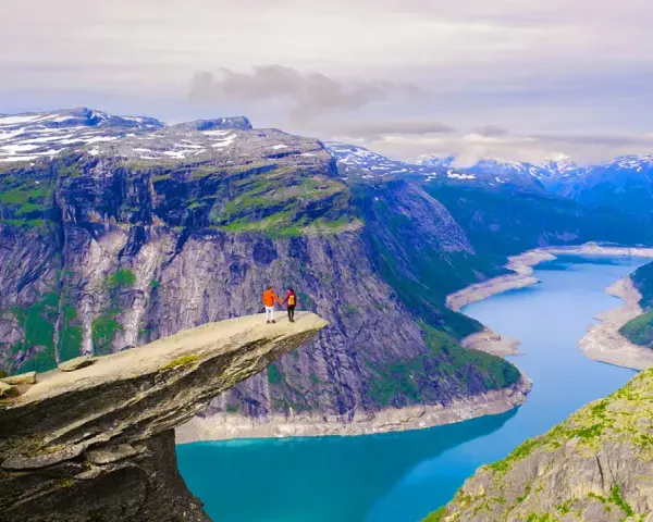 Två personer står på Trolltunga, en klippavsats i Norge, med en fantastisk utsikt över bergen och naturen.