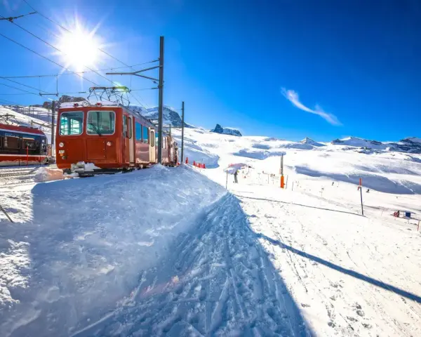 Ett snötäckt tåg i Schweiz, redo att transportera skidåkare uppför berget under en strålande solig dag.