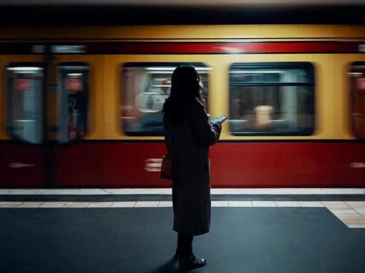 Kvinna med mobil på perrongen i Berlin, en gul och röd tunnelbanevagn susar förbi. Perfekt för din berlin reseguide.