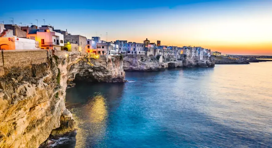 Solnedgång över Polignano a Mare, en pittoresk kuststad i Puglia, Italien. Vita hus klättrar på klipporna ovanför det turkosblå havet.