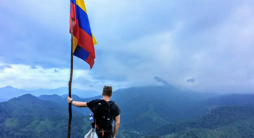 Vandrare med Colombias flagga på en bergstopp. Trots ryktet om att en resa till Colombia kan vara farligt, njuter han av den dramatiska utsikten.