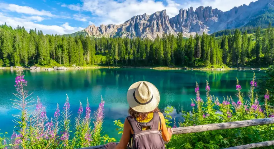 En kvinna med hatt och ryggsäck njuter av en vacker sommardag vid en turkos sjö i Dolomiterna.
