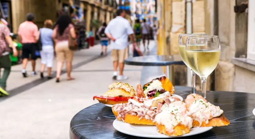 Tapas och vin på en uteservering i San Sebastián. Folk promenerar förbi på den livliga gatan.