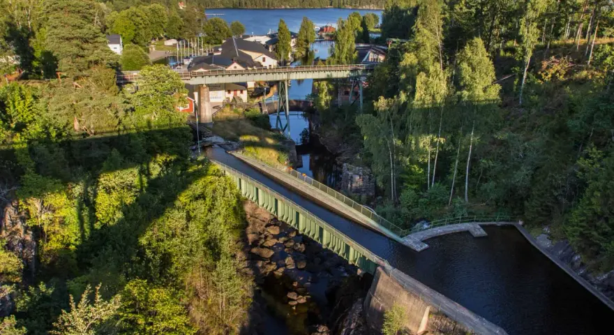 Vattenvägar och akvedukter i Sverige, med gröna broar som leder vatten över en ravin, omgivna av frodig skog och en sjö i bakgrunden.