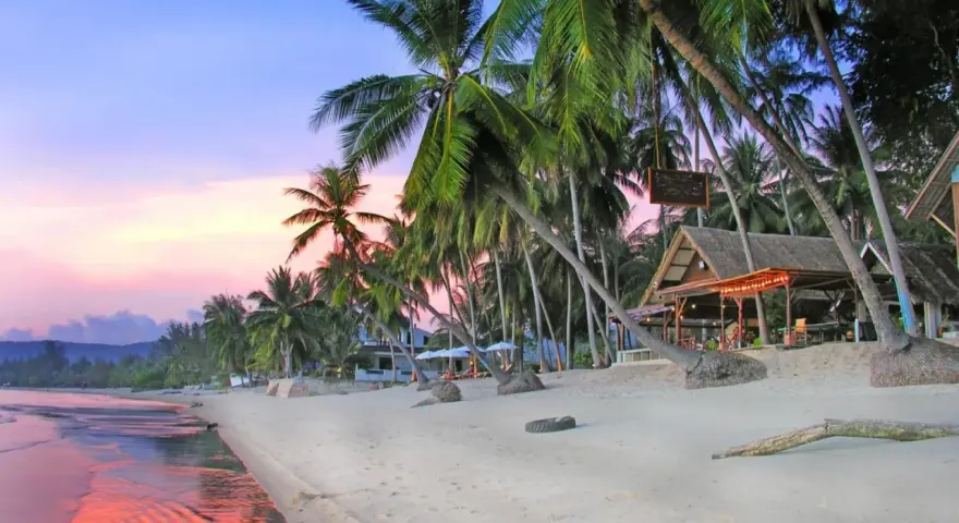 En vacker strand på Koh Samui, Thailand, med vajande palmer, en strandbar och ett hav som speglar den rosa solnedgången.