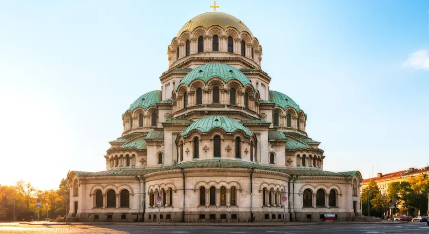 Imponerande kyrka med gröna kupoler och ett gyllene kors i Sofia, Bulgarien. En vacker syn i morgonsolen.