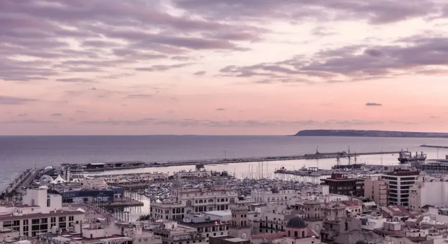 En vacker solnedgång över hamnen i Alicante i december. Molnen färgas i rosa och lila över havet och staden.