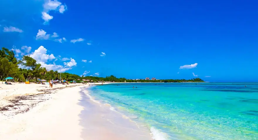 Vacker strand med turkost vatten och vita moln. Trots den idylliska vyn, kan Playa del Carmen vara farligt.