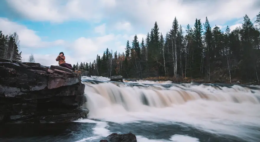 Person sitter på en klippa vid ett forsande vattenfall i Dalarna, ett perfekt utflyktsmål.