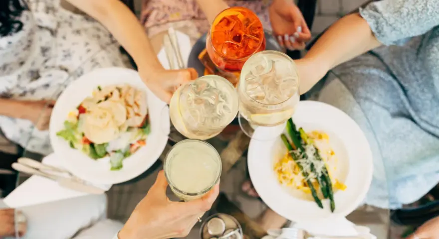 Vänner skålar med drinkar och njuter av en härlig milano mat-upplevelse med sallad och pasta med sparris.
