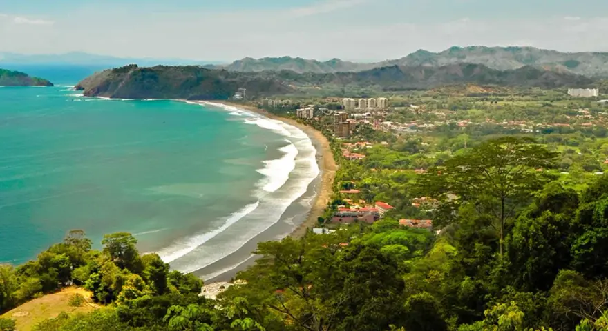 Vacker kustlinje med turkost hav, vågor som slår mot en sandstrand och frodig grönska som omger en stad. En dröm om en costa rica strand.