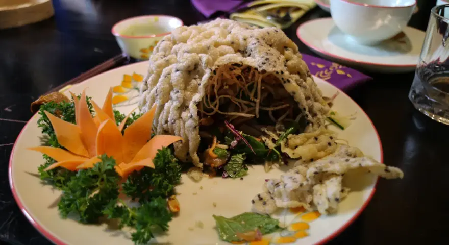 En vacker vietnamesisk maträtt med krispig rispapperstäckt sallad, dekorerad med morotsblomma och örter.