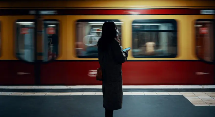 Kvinna med mobil på perrongen i Berlin, en gul och röd tunnelbanevagn susar förbi. Perfekt för din berlin reseguide.