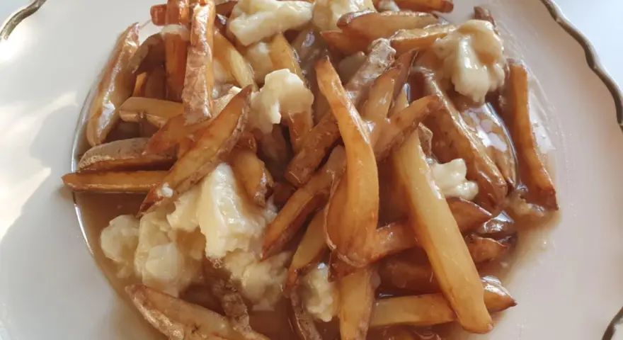 En tallrik med kanadas nationalrätt, poutine: friterade pommes frites, ostbitar och sås.