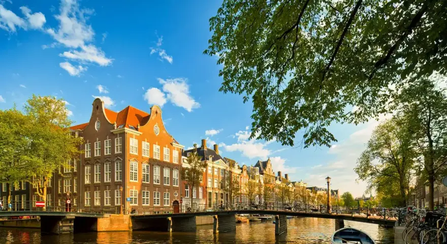 En vacker kanalvy i Amsterdam med klassiska hus, broar och båtar. Perfekt för din amsterdam reseguide.