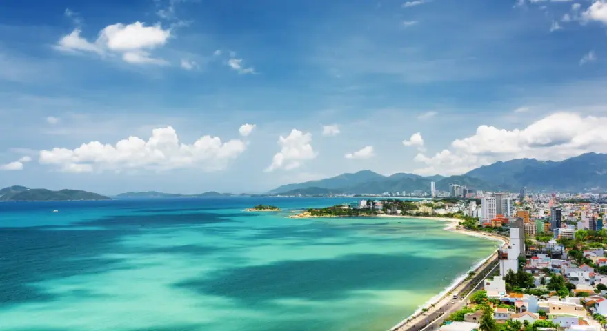 Vacker vy över Nha Trang, Vietnam, med turkost vatten, gröna kullar och en stad vid kusten under en blå himmel med moln.
