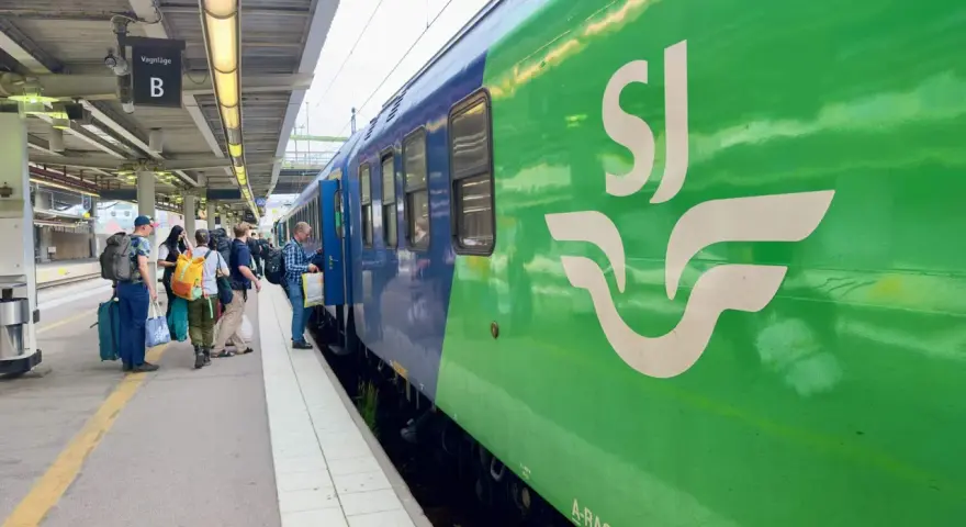Folk väntar på perrongen vid vagnhall B. Ett grönt SJ-tåg står redo för resan, kanske till och med ett tåg till London.