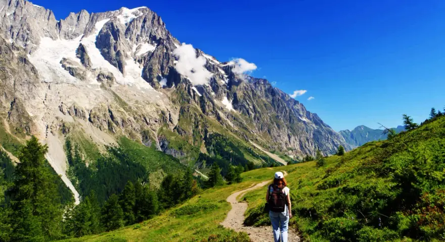 En person vandrar på en stig i Chamonix med majestätiska berg och en glaciär i bakgrunden.