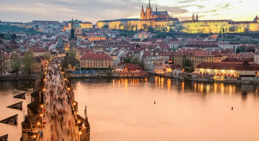 En livlig kväll på Karlsbron i Prag, med tusentals besökare som promenerar mot slottet. En perfekt vy för den som tar tåg till Prag.
