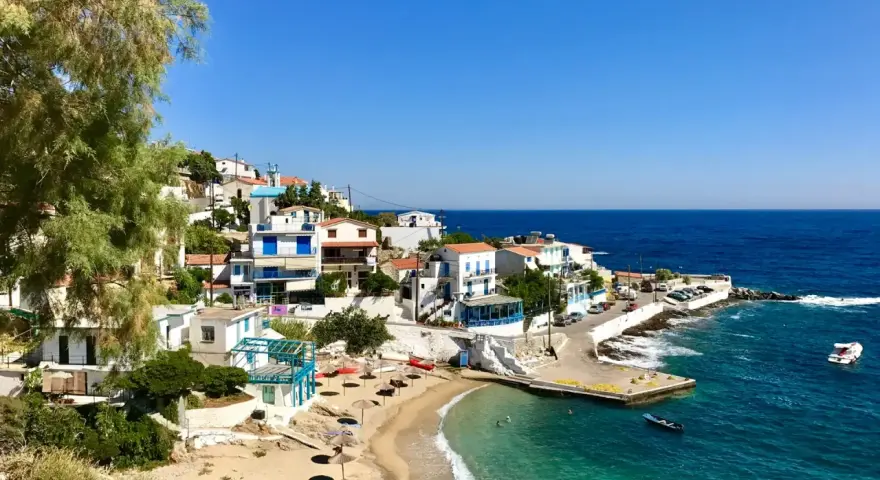 En pittoresk kustby på Ikaria, Grekland, med vita hus, en sandstrand och turkost vatten.