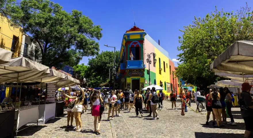 Färgglada hus och marknadsstånd i Buenos Aires. En livlig gata med människor som njuter av solen.