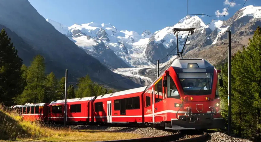 Ett rött tåg slingrar sig fram genom ett dramatiskt alplandskap med snöklädda berg. Kanske är det ett tåg till Italien, med hisnande vyer längs vägen.
