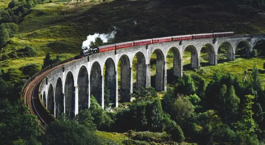 Ångloket på Glenfinnanviadukten i Skottland, som påminner om Harry Potter tåg skottland, ångar fram över den gröna dalen.