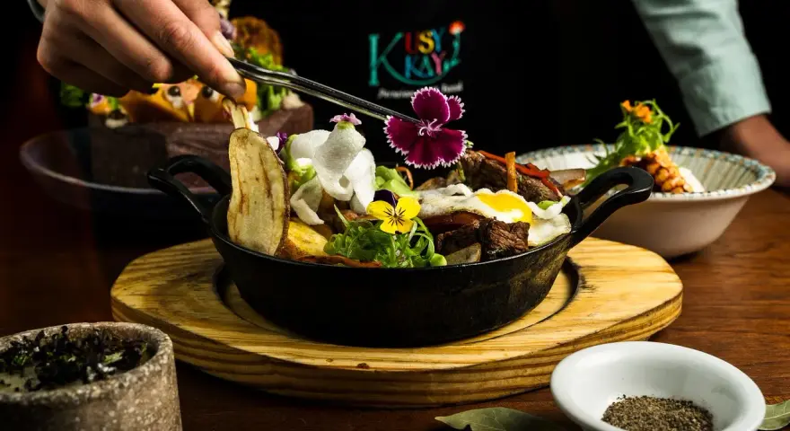 En hand dekorerar en mustig gryta med kött, potatis och blommor. En utsökt rätt som påminner om kanadensiskt kök.