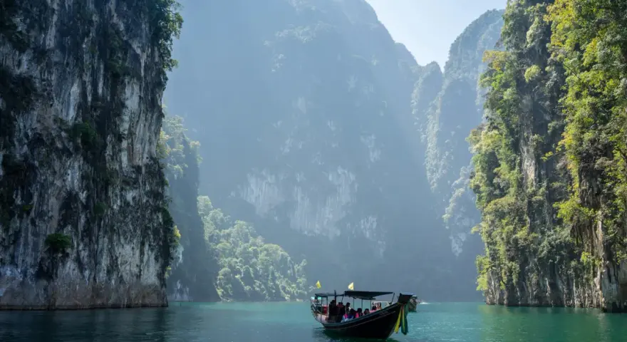 En båt färdas på turkost vatten genom dramatiska kalkstensklippor i Khao Sok nationalpark.